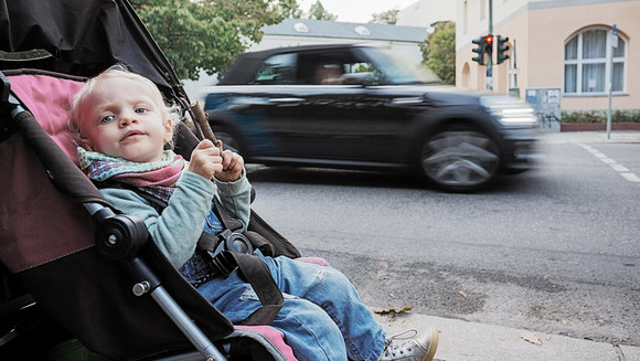 Ein kleines Kind sitzt im Kinderwagen am Straßenrand