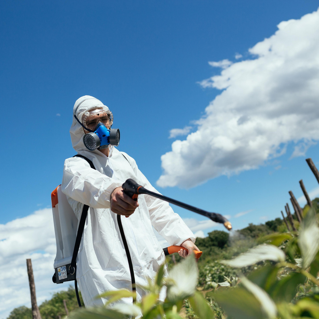 Person in Schutzanzug bringt Pestizide auf Feld aus
