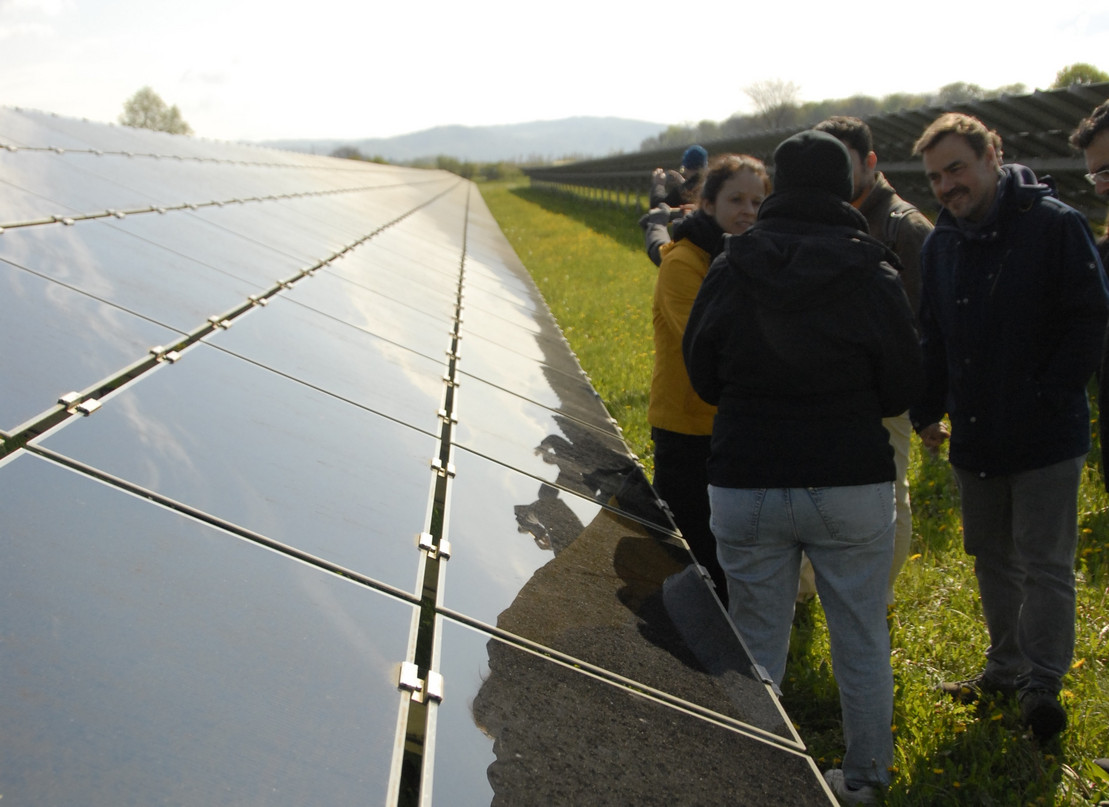 Eine Gruppe von Menschen steht neben einer Freiflächen-Photovoltaikanlage und unterhält sich.
