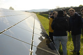 Eine Gruppe von Menschen steht neben einer PV-Freiflächenanlage und unterhält sich.