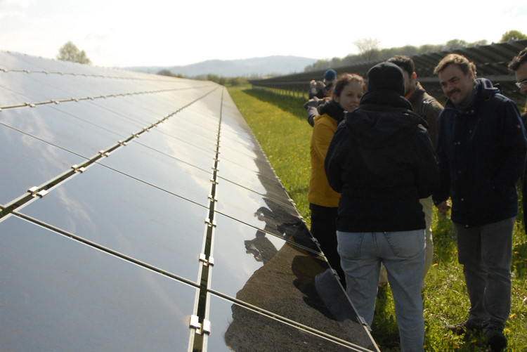 Eine Gruppe von Menschen steht neben einer PV-Freiflächenanlage und unterhält sich.